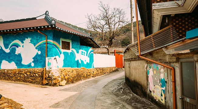 파란 벽화가 그려진 한옥 담장과 좁은 골목길, 겨울 나무와 어우러진 포근한 마을 풍경