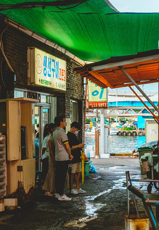 초록 차양 아래 가게 앞에서 손님을 맞이하는 생선구이 노포의 정겨운 풍경