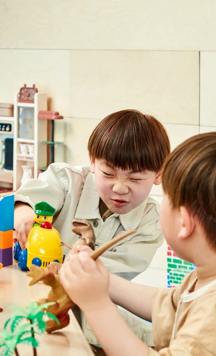 테이블에서 공룡과 블록 장난감을 가지고 진지하게 집중하며 노는 두 아이