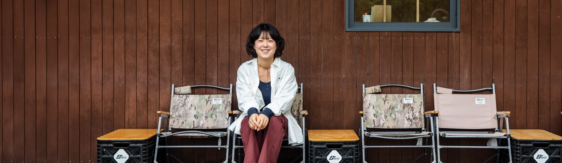 제주 애월 소길별하 야외 원목 벽 앞 캠핑 의자에 앉아 환하게 미소 짓는 윤자연 책임 매니저의 모습