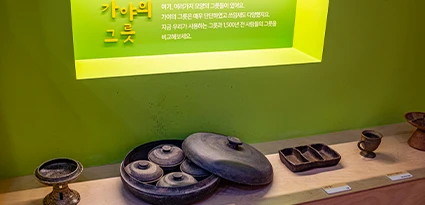 초록빛 조명 아래 가야 사람들이 쓰던 토기와 그릇들이 나란히 전시된 진열대