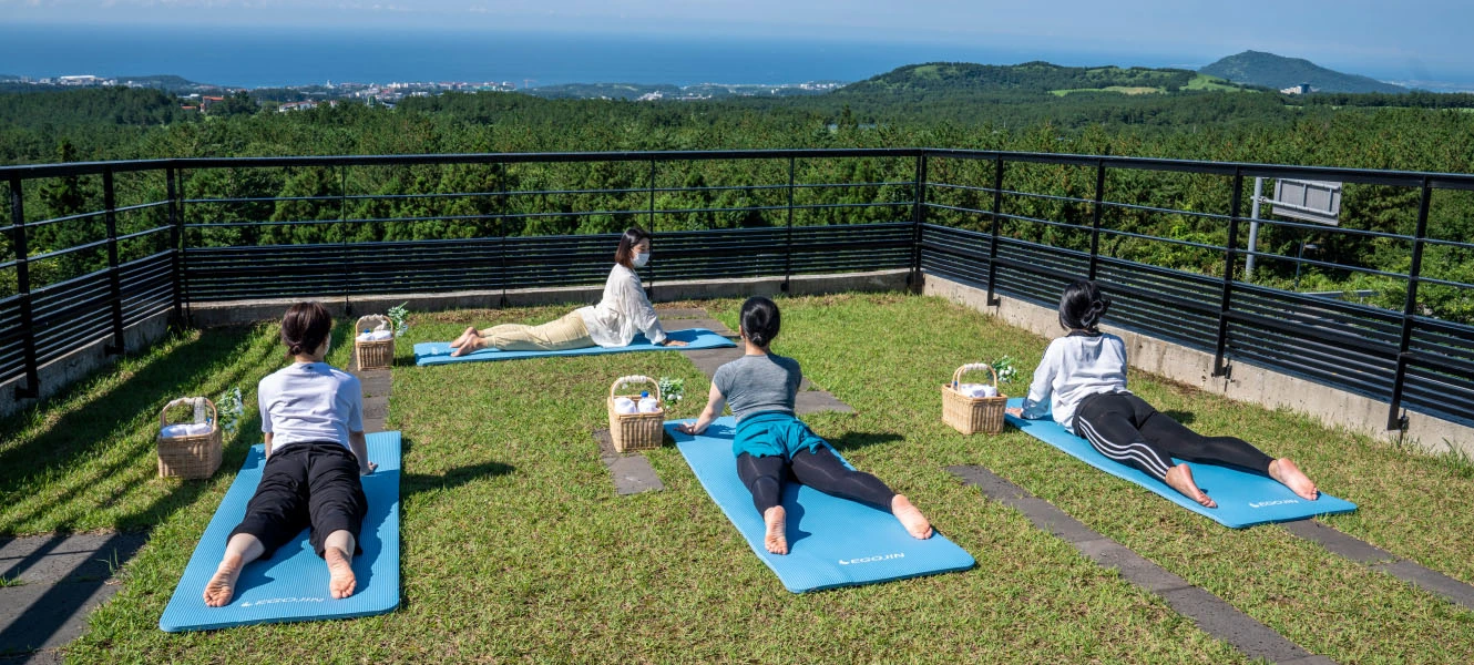 전망대 잔디밭에서 참가자가 매트에 앉아 한쪽 다리를 뻗는 런지 스트레칭을 하는 모습