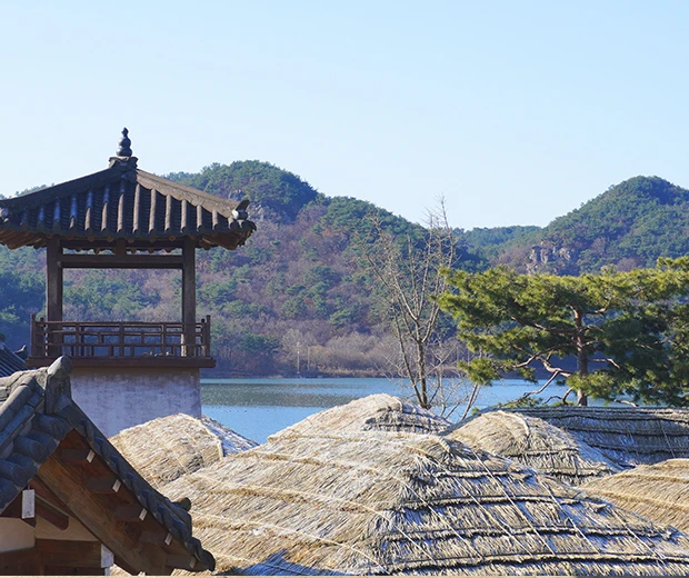초가지붕 너머 망루와 덕용 저수지, 야트막한 산이 펼쳐진 서동요 테마파크의 겨울 전망