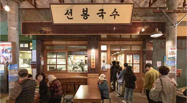 선봉국수 노란 간판 아래 손님들이 줄지어 기다리는 가게 외관