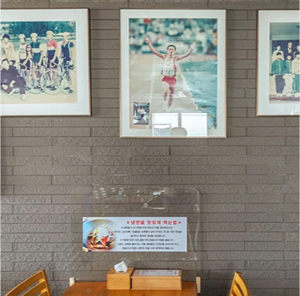 벽돌 벽에 마라톤 우승 사진 등 액자가 걸린 함흥냉면옥 내부와 냉면 안내문