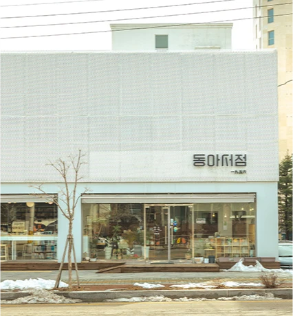 흰 외벽에 동아서점 간판이 걸린 단정한 건물 외관, 앞쪽에 잔설과 앙상한 나무가 보인다