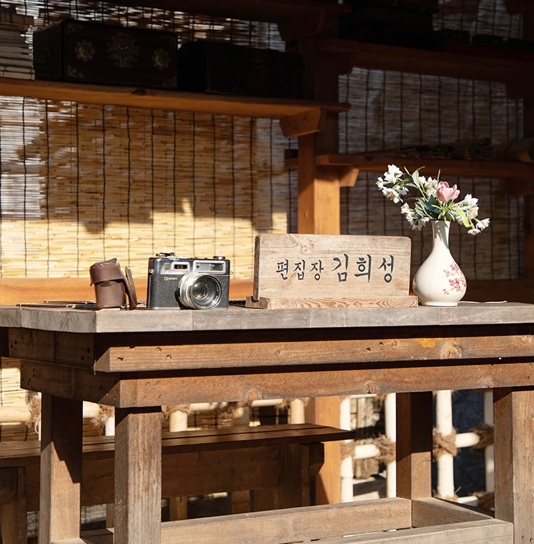 발을 친 목조 공간에 옛 필름 카메라와 편집장 김희성 명패, 백자 꽃병이 놓인 햇살 든 책상
