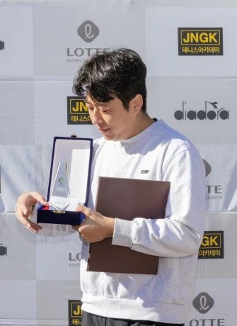 포토월 앞에서 케이스에 담긴 상패를 받아 들고 바라보는 남성 수상자