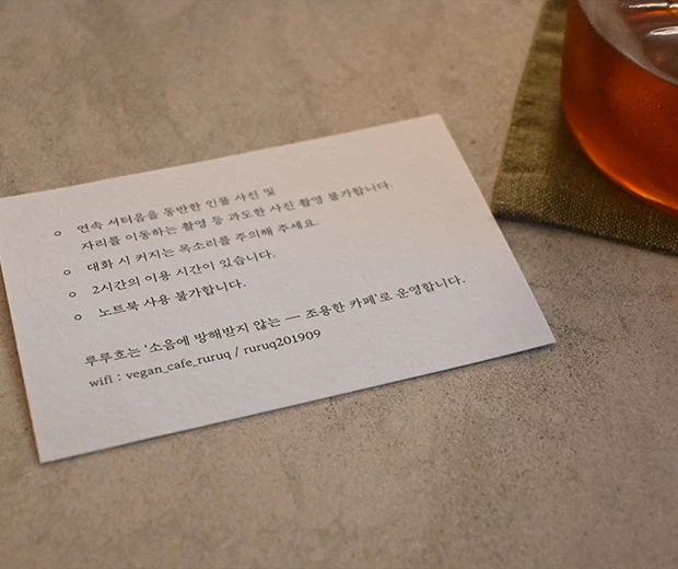 삼베 코스터 위 홍차 한 잔 옆에 놓인 루루흐의 조용한 카페 이용 안내 카드