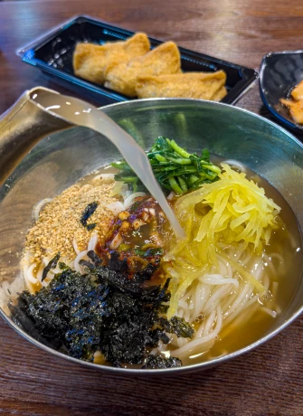 참기름 깨 김 단무지 부추를 올린 멸치국수에 육수를 부어 완성하는 모습과 곁들인 유부