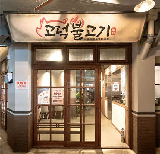 불꽃 로고가 그려진 고덕불고기 간판과 유리문 너머로 보이는 매장 입구