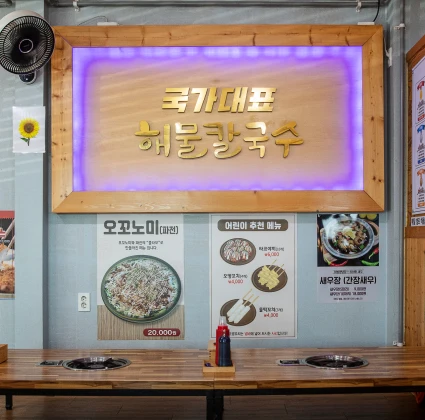 국가대표 해물칼국수 식당 내부, 환하게 빛나는 메뉴 간판과 화구가 놓인 테이블