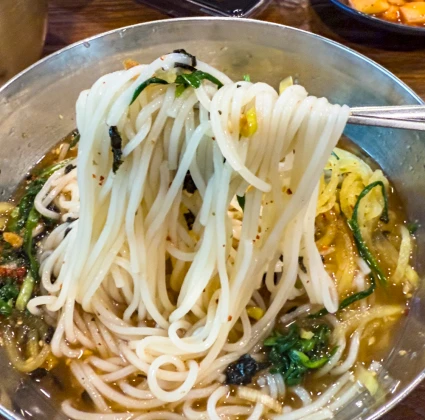 젓가락으로 집어 올린 하얀 중면 국수 가닥과 부추가 어우러진 멸치국수 한 그릇