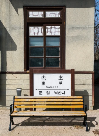 속초 한자 역명판이 붙은 옛 건물 창문 아래 놓인 원목 벤치, 레트로 감성의 거리 한 켠