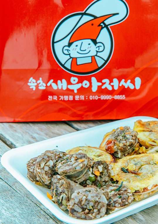 속초새우아저씨 빨간 포장 봉투 앞 흰 접시에 담긴 오징어순대와 아바이순대