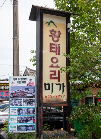 초록 산 그림이 그려진 황태요리 미가 식당의 노란 입간판, 아래에 메뉴 안내판이 붙어 있는 모습