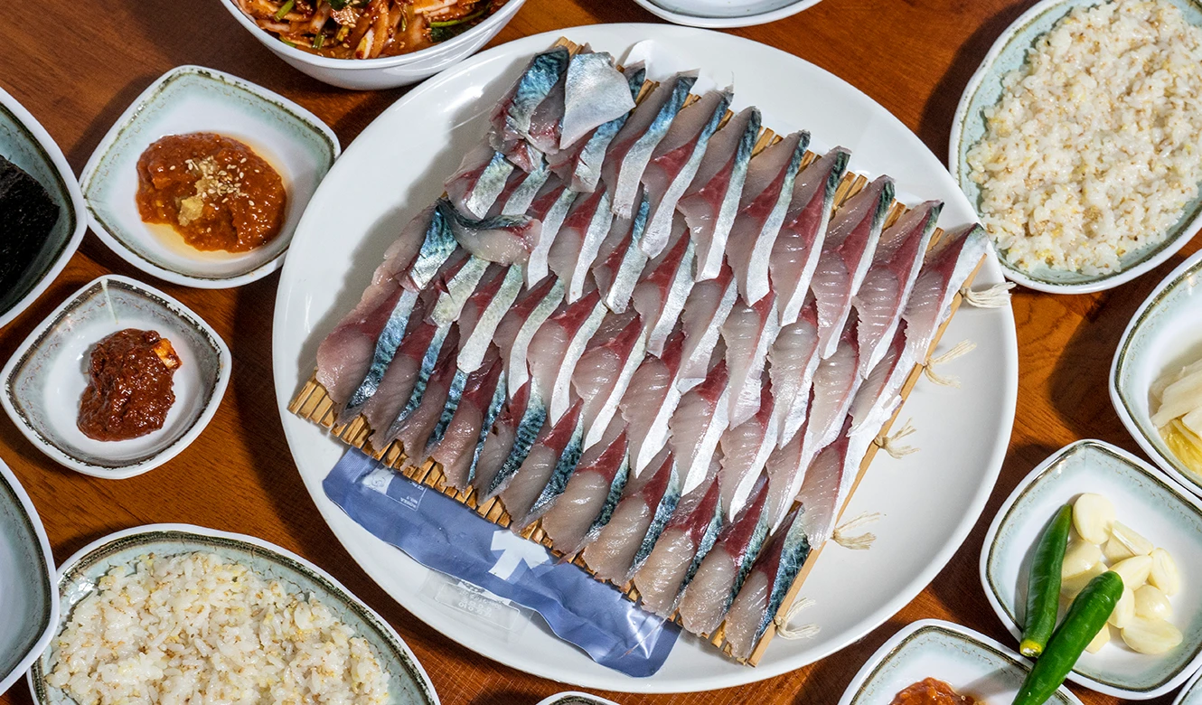 흰 접시에 가지런히 저며 담은 고등어회와 곁들인 밥, 여러 밑반찬이 차려진 한 상