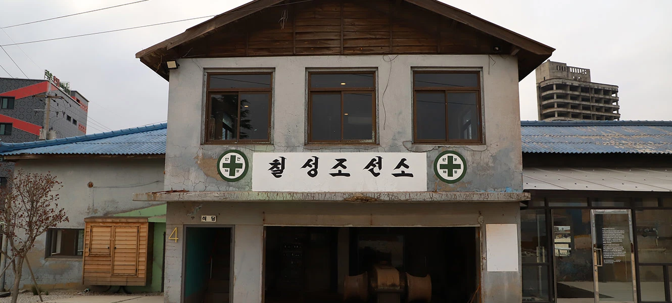 흐린 하늘 아래 칠성조선소 간판이 걸린 낡은 이층 건물 외관과 주변 거리 풍경
