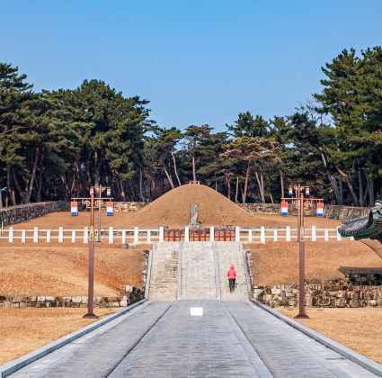 긴 돌길 끝 둥근 봉분으로 이어지는 수로왕릉 진입로를 붉은 옷을 입은 사람이 걸어 오르는 풍경