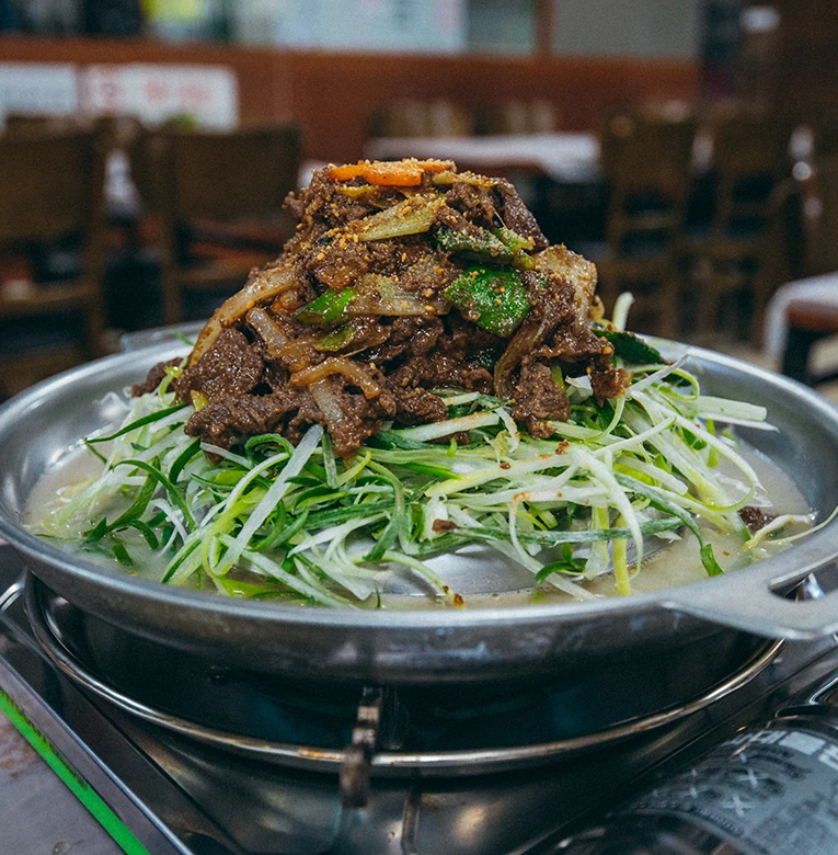 채 썬 오이를 푸짐하게 깔고 양념 고기를 올린 파불고기가 가스불 위 냄비에 담긴 모습