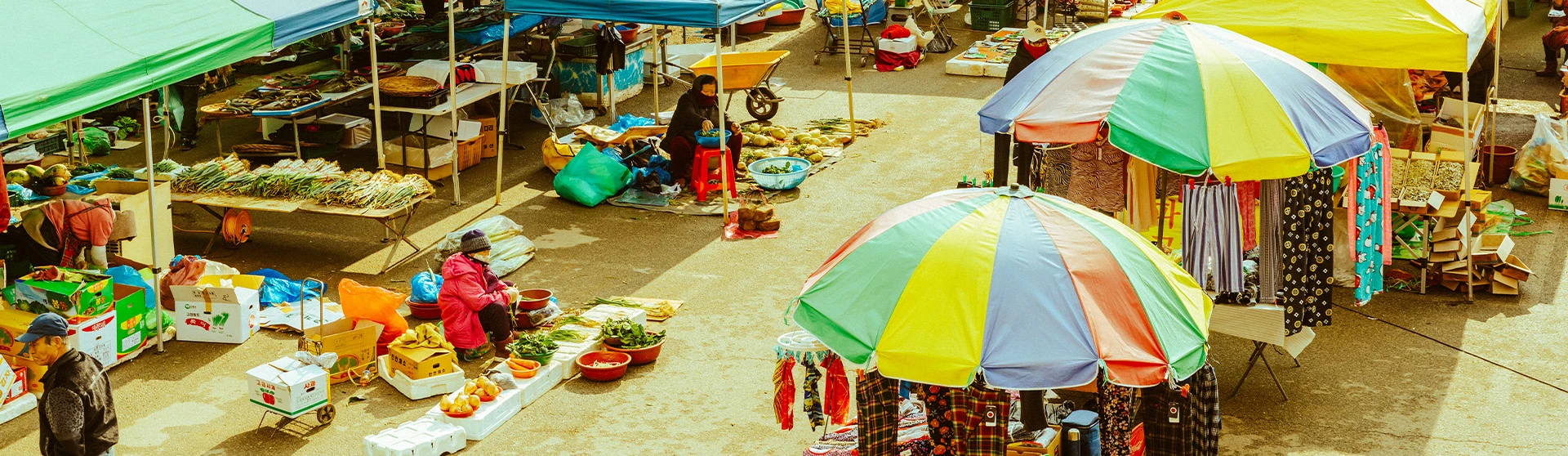 위에서 내려다본 부여 오일장 전경. 빨강·노랑·파랑 줄무늬 파라솔과 천막 아래로 채소와 과일을 담은 좌판이 늘어서 있고 상인과 손님들이 오가고 있다