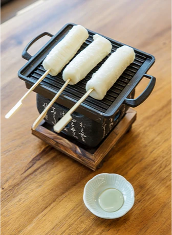 작은 무쇠 그릴 위에 가래떡 꼬치 세 개가 나란히 구워지고, 옆에는 조청을 담은 흰 종지가 놓여 있다