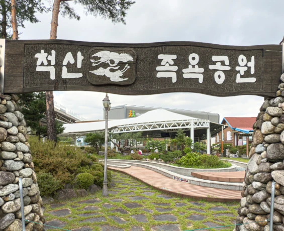 통나무에 척산 족욕공원이라 새긴 간판과 돌기둥, 그 너머 흰 차양 정자가 보이는 입구