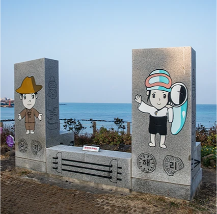 바닷가에 세운 두 돌기둥에 어부와 해녀 소년 캐릭터가 그려진 마을 조형물