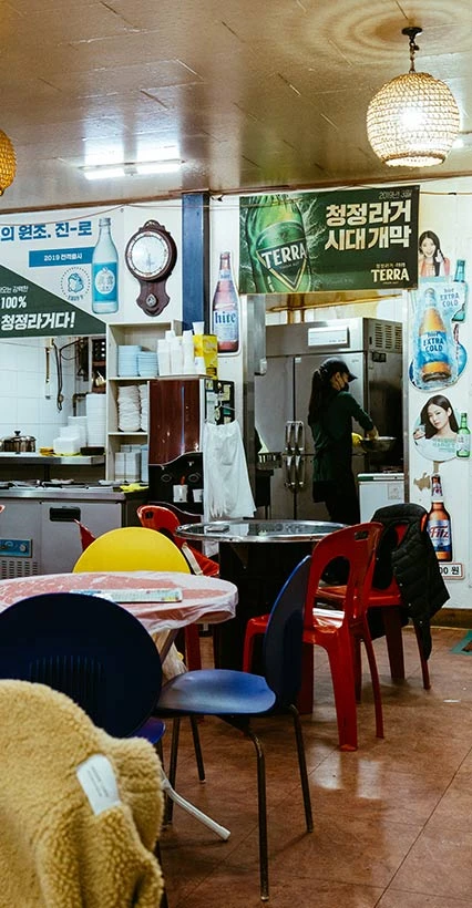 소주 포스터와 플라스틱 의자가 놓인 정겨운 포장마차 식당 내부, 안쪽 주방에서 일하는 모습