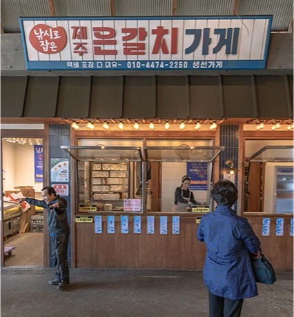 제주 은갈치 가게 간판 앞에서 직원과 손님이 마주한 생선 가게 풍경