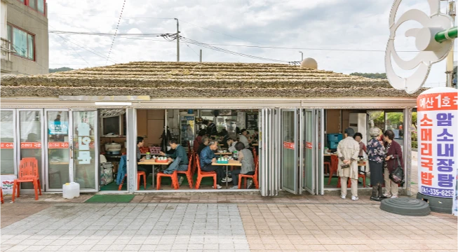 초가 처마 아래 통유리 안에서 손님들이 식사하는 예산 국밥집 외관