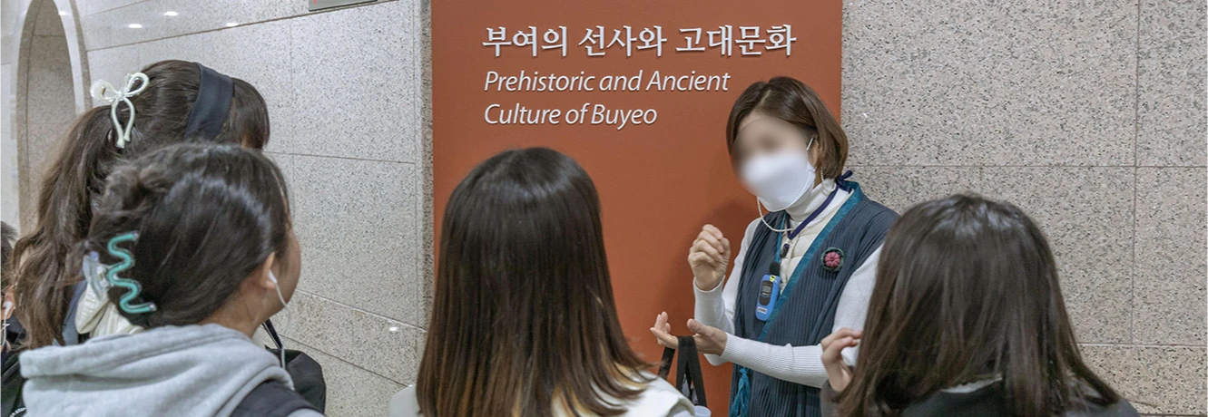 부여의 선사와 고대문화 안내판 앞에서 해설사가 아이들에게 전시를 설명하는 모습