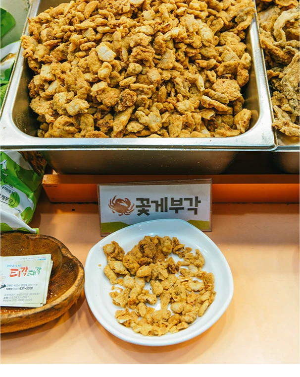 매대 위에 수북이 쌓인 꽃게부각과 접시에 덜어 놓은 노릇한 시식용 부각