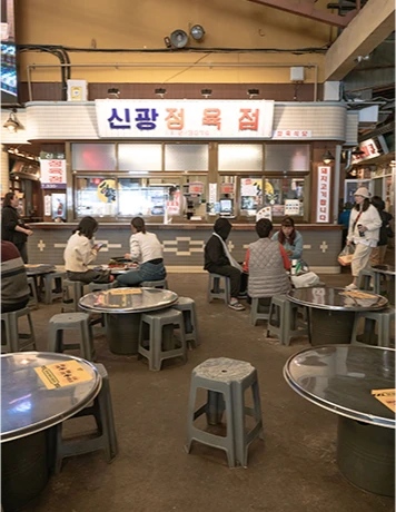 신광정육점 간판 아래 둥근 테이블과 플라스틱 의자가 놓인 한산한 광장 식사 공간