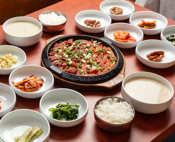 원목 식탁 가운데 양념 황태구이가 담긴 무쇠 판을 두고 흰 그릇의 밑반찬과 황태국, 공기밥이 둥글게 차려진 한 상