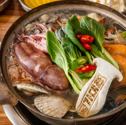 통오징어와 조개, 청경채, 송이버섯, 붉은 고추가 어우러진 해물칼국수 전골 클로즈업