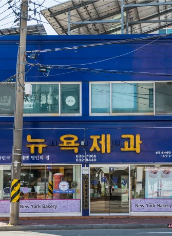 파란 외벽에 뉴욕제과 간판을 단 2층 건물, 전선이 가로지르는 속초 거리의 노포 빵집 전경