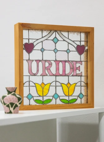 하트와 노란 튤립 문양에 URIDE 글자를 넣은 스테인드글라스 작품을 나무 액자에 담아 세워둔 모습