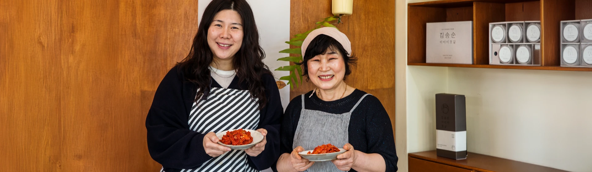 앞치마를 두른 정가영 대표와 김송순 명인이 가자미식해를 담은 접시를 들고 매장에서 환하게 웃고 있는 모습