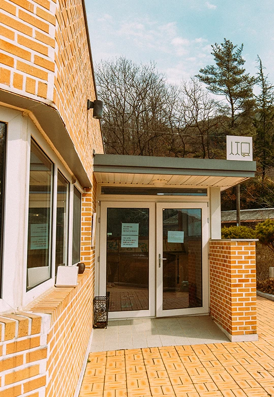 벽돌로 지은 찻집 건물의 유리문 입구, 뒤로 야트막한 산이 보이는 마을 초입 풍경