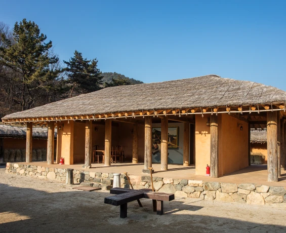 흙벽과 나무 기둥, 돌 기단으로 지은 너른 초가집 가옥 앞에 평상이 놓여 있는 생활문화마을의 한 채