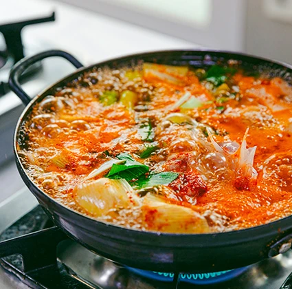 검은 전골냄비에서 채소와 파를 넣고 얼큰하게 끓고 있는 붉은 국물의 곰치국