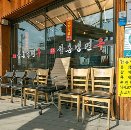 유리문에 붉은 상호가 적힌 함흥냉면옥 입구, 영업 전 의자들을 내놓은 가게 앞