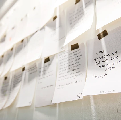 벽에 줄을 매어 집게로 걸어 둔 손글씨 방명록들. 방문객이 남긴 메모가 빼곡하게 걸려 있고 한 장에는 2025년 날짜가 적혀 있다.
