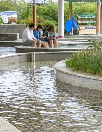 족욕공원 정자 아래 사람들이 둘러앉아 물에 발을 담그고 쉬는 모습과 자갈 깔린 족욕탕