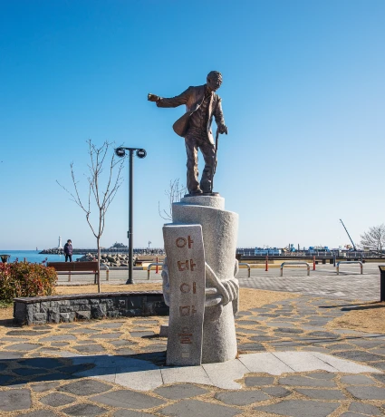 속초 아바이마을 부둣가에 세워진, 짐을 진 아바이를 형상화한 동상과 맑은 하늘 아래 펼쳐진 항구 풍경