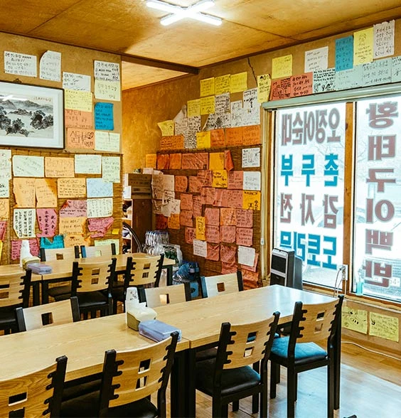 벽면 가득 여행객들이 남긴 손글씨 메모로 채워진 순자집 곰치국 식당 내부의 원목 식탁들