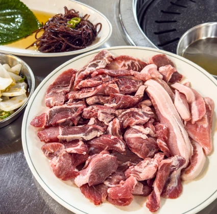 흰 접시에 푸짐하게 담긴 신선한 뒷고기 모둠과 곁들이 채소, 무생채가 차려진 모습