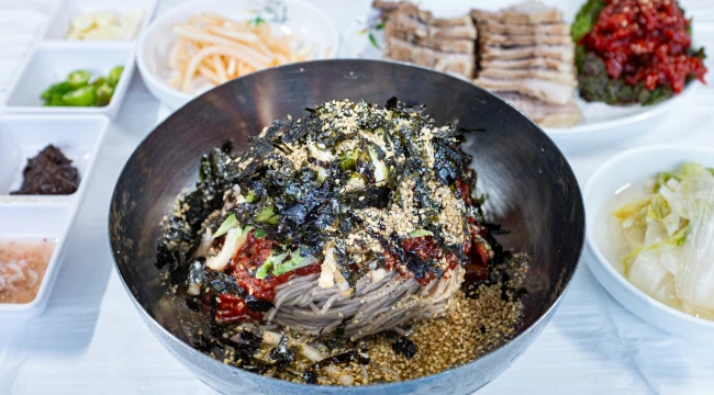 양푼에 김가루를 듬뿍 올린 비빔막국수와 수육, 양념, 백김치가 함께 차려진 푸짐한 한 상