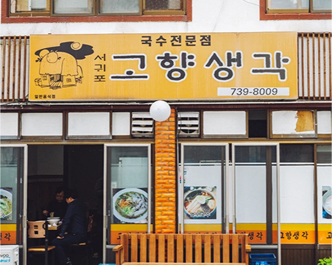 서귀포 고향생각 국수전문점의 노란 간판과 손님이 앉아 있는 가게 외관